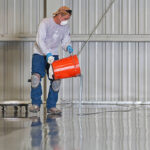 A construction worker pours paint onto a warehouse floor.