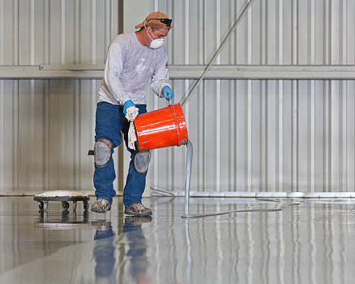 A construction worker pours paint onto a warehouse floor.