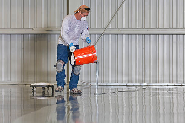 A construction worker pours paint onto a warehouse floor.